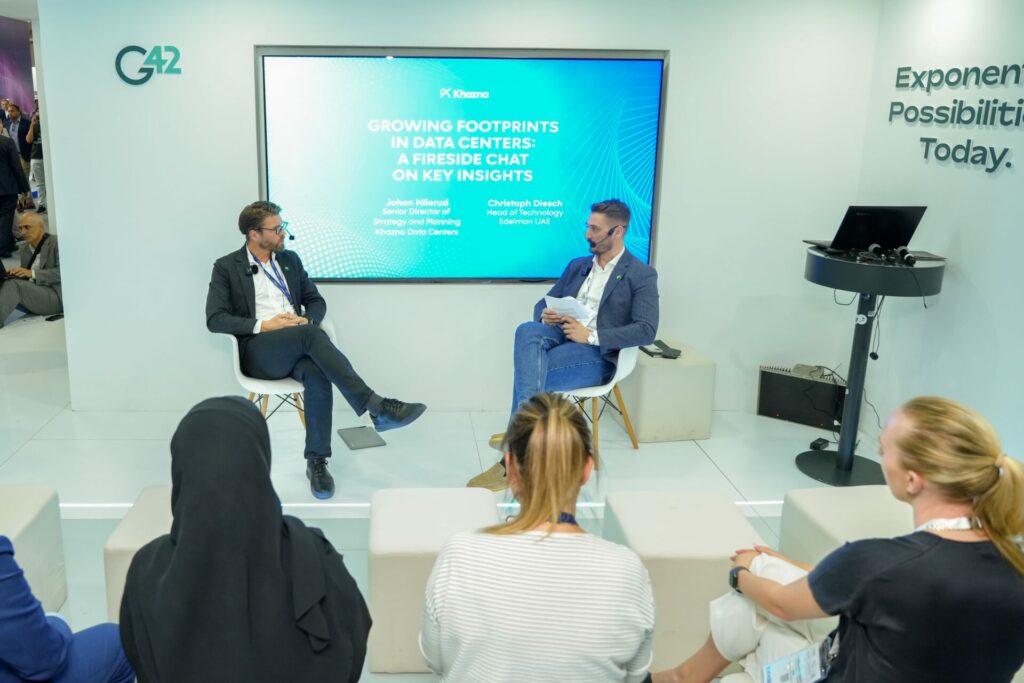 Two speakers engaged in a fireside chat at GITEX, discussing Khazna Data Centers' recently launched whitepaper. Seated in front of a screen, they address the audience, sharing insights and knowledge during this informative session